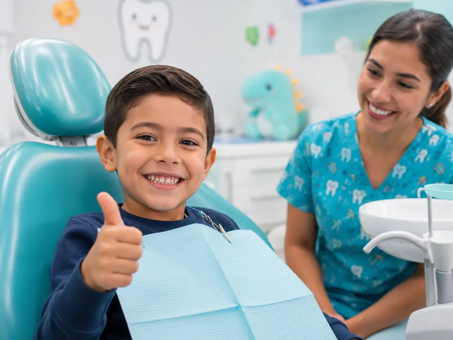 Niño sonriendo con el pulgar arriba en el sillón dental junto a la odontopediatra